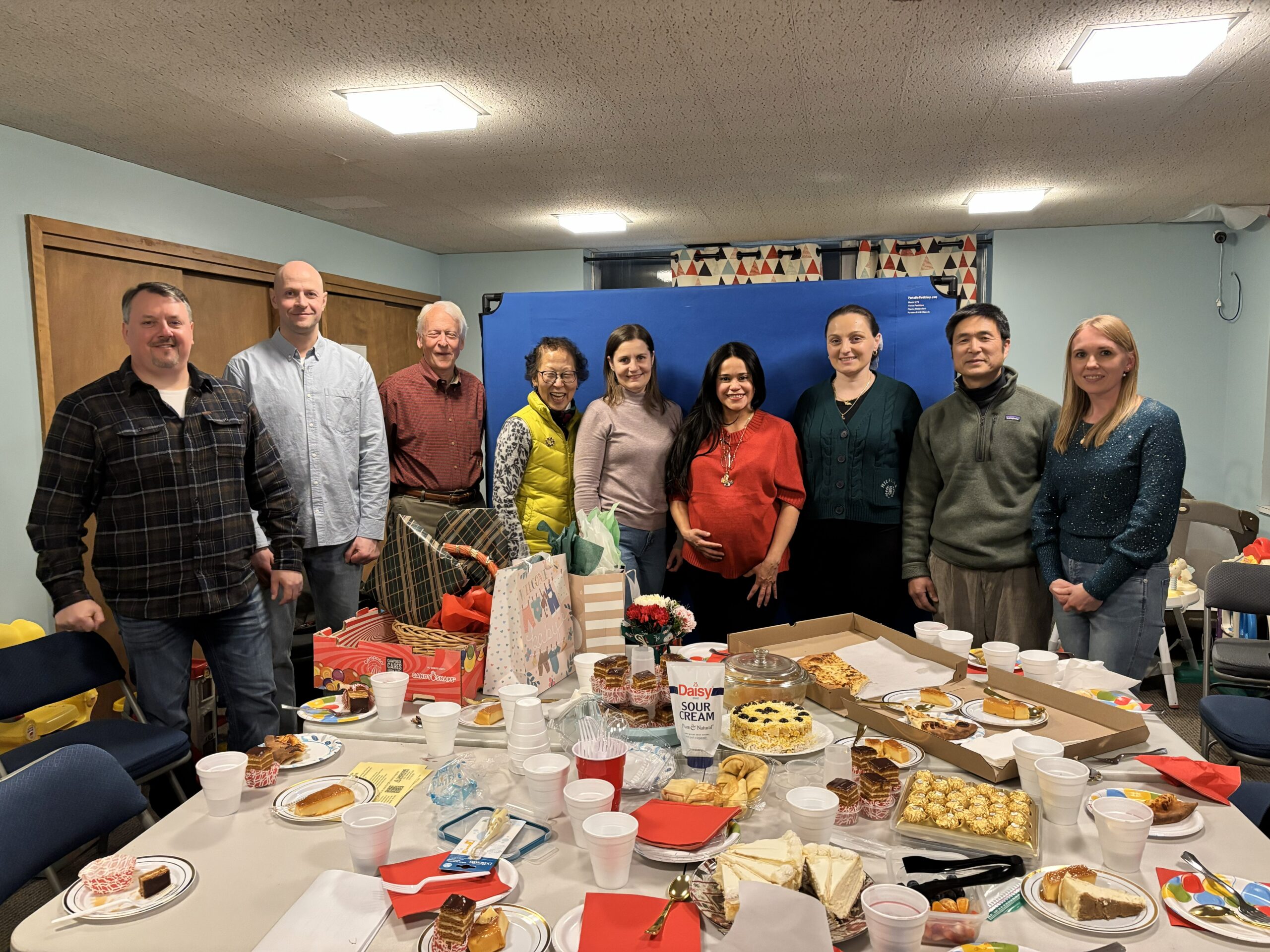 A group of people standing infront of a table full of food during a baby shower