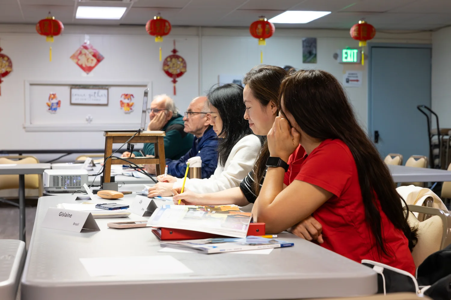 A group of students listening to an ESL lesson with their workbooks open infront of them.